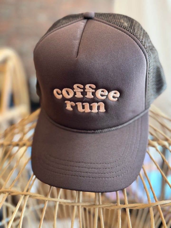 A brown and beige trucker hat with the words "coffee run" displayed prominently on the front in a tan color, showcasing a casual and chic style. Perfect for everyday wear and adding a trendy touch to your coffee runs. Available at Maven Blush Boutique.