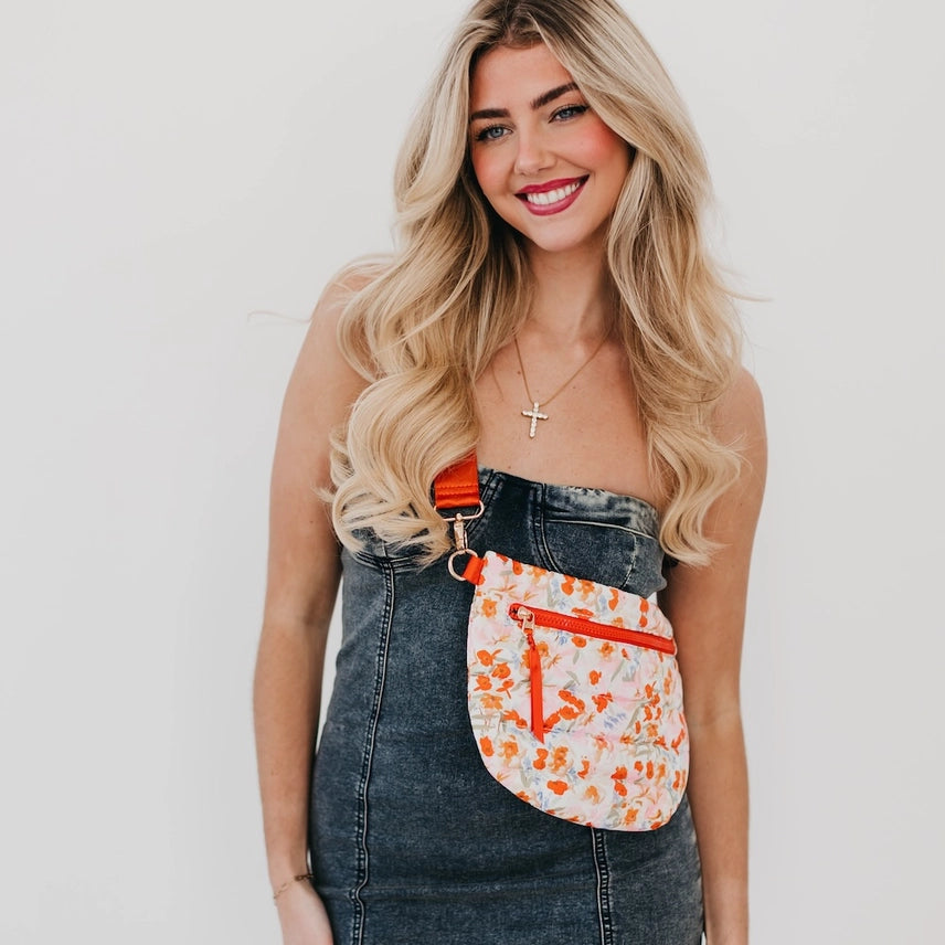 A vibrant orange floral Jolie Puffer Belt Bag with a puffer-textured design, gold hardware, and an adjustable strap. Can be worn as a belt bag, crossbody, or shoulder bag for hands-free convenience.