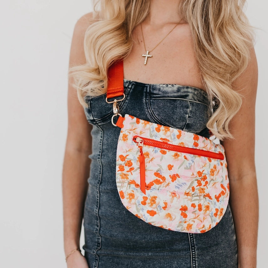 A vibrant orange floral Jolie Puffer Belt Bag with a puffer-textured design, gold hardware, and an adjustable strap. Can be worn as a belt bag, crossbody, or shoulder bag for hands-free convenience.