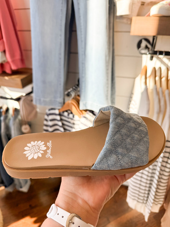 Sanibel Denim Slide Sandal with puffy quilted straps and a cushioned footbed, designed for effortless everyday wear. Light denim color.