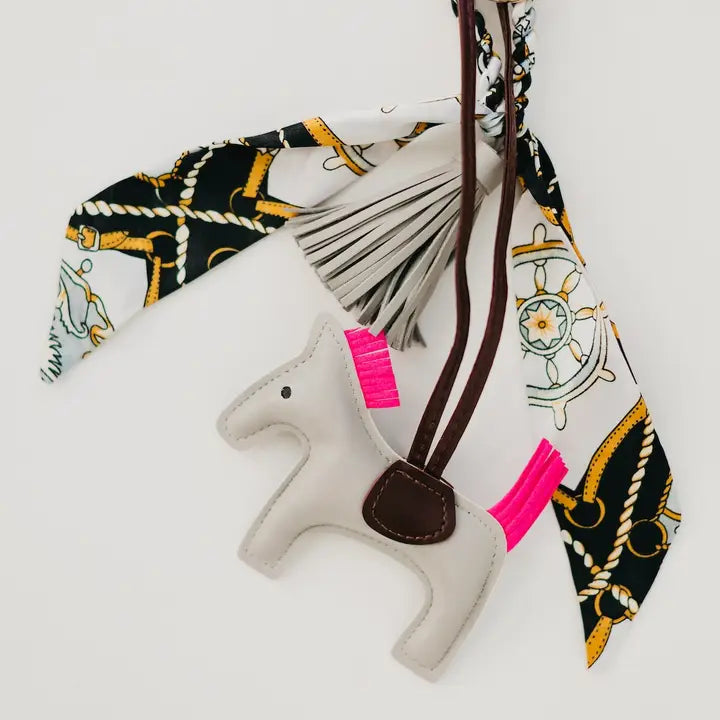 Secretariat Bag Charm with a horse pendant, mini silk scarf, and tassel, designed as a stylish add-on for handbags and totes. Available in tan or gray. Photo of the bag charm in gray.