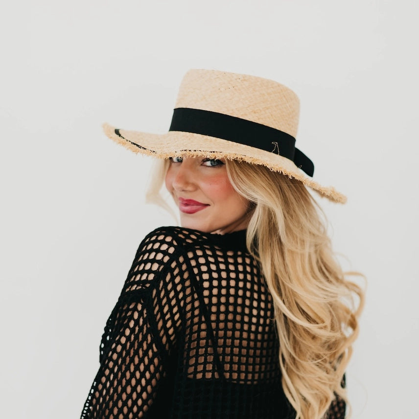 Woman wearing raffia sun hat with black ribbon and fringe brim.