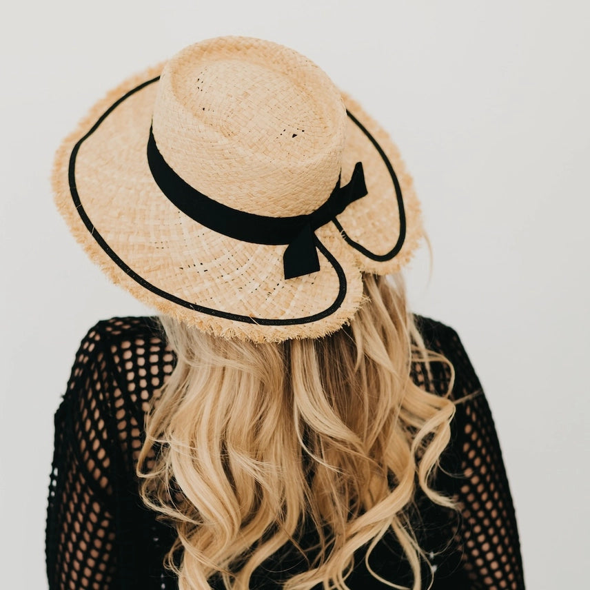 Woman wearing raffia sun hat with black ribbon and fringe brim, back view.