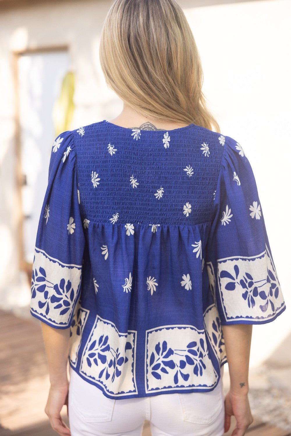 Back view of royal blue smocked floral top with short sleeves and block print design, styled for everyday or office wear. Brand Voy.