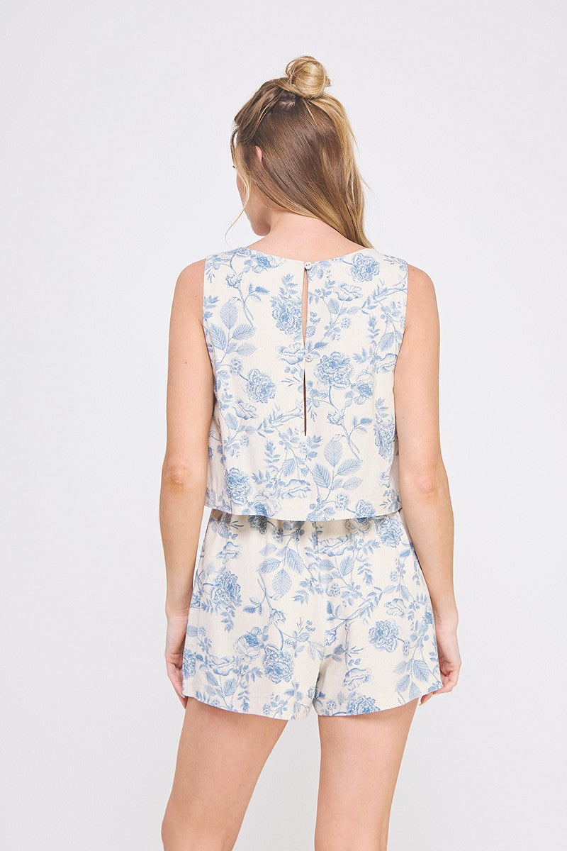 Back view of Nia linen short romper in blue and cream toile print with square neckline, faux tie waist, and overlay detail.