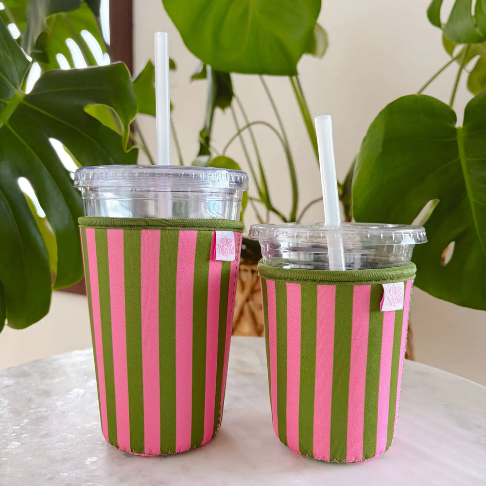 Two iced coffees in pink and green striped reusable sip sleeves on a white table