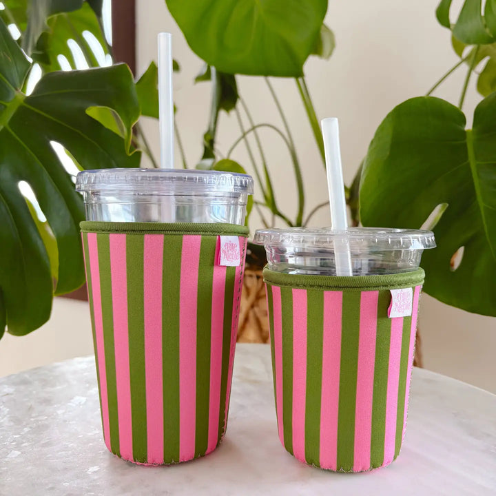 Two iced coffees in pink and green striped reusable sip sleeves on a white table