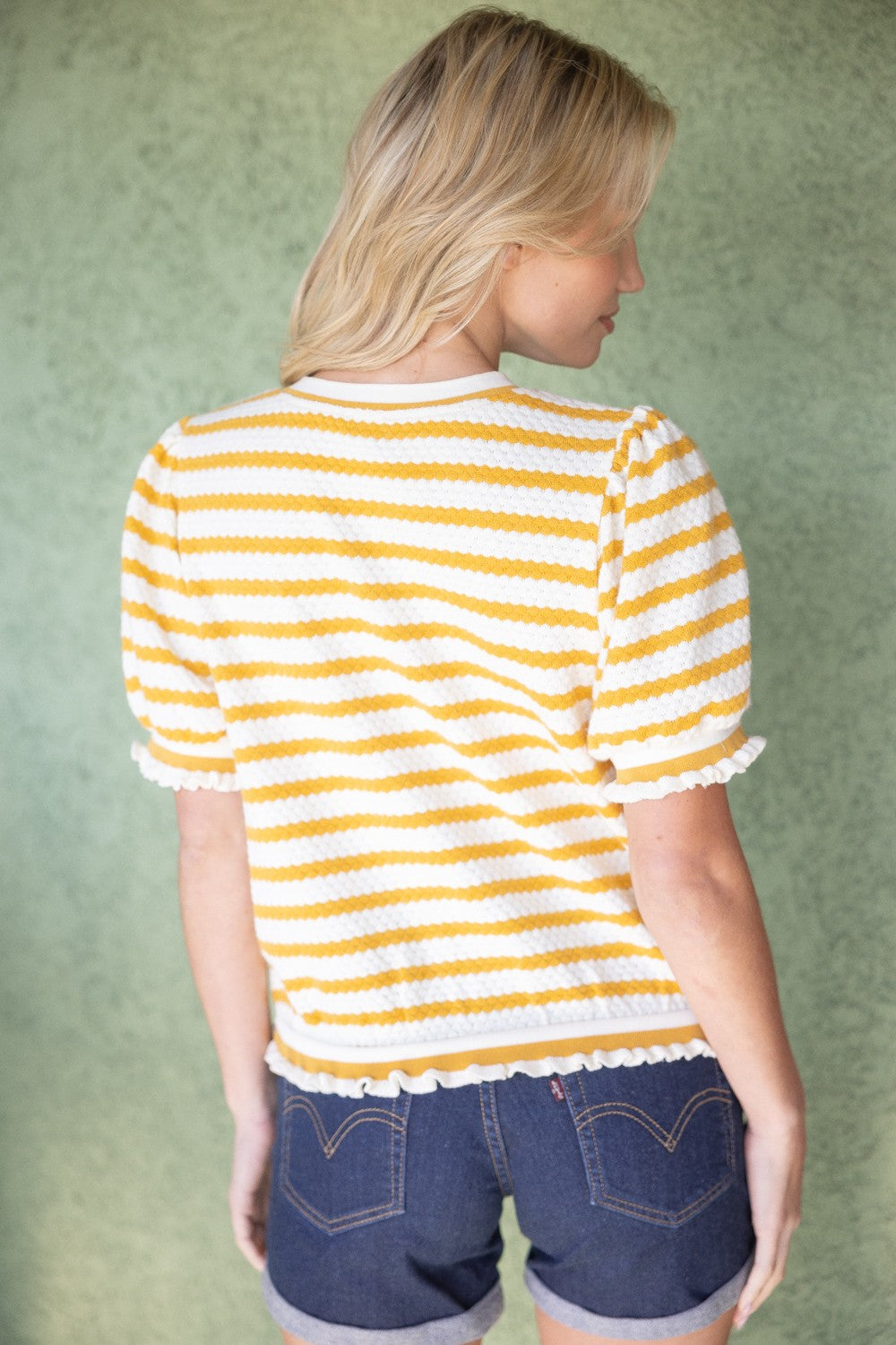 Back view of mustard and white striped knit short sleeve blouse with ruffle trim, styled as a casual work top for women. Top by Voy.